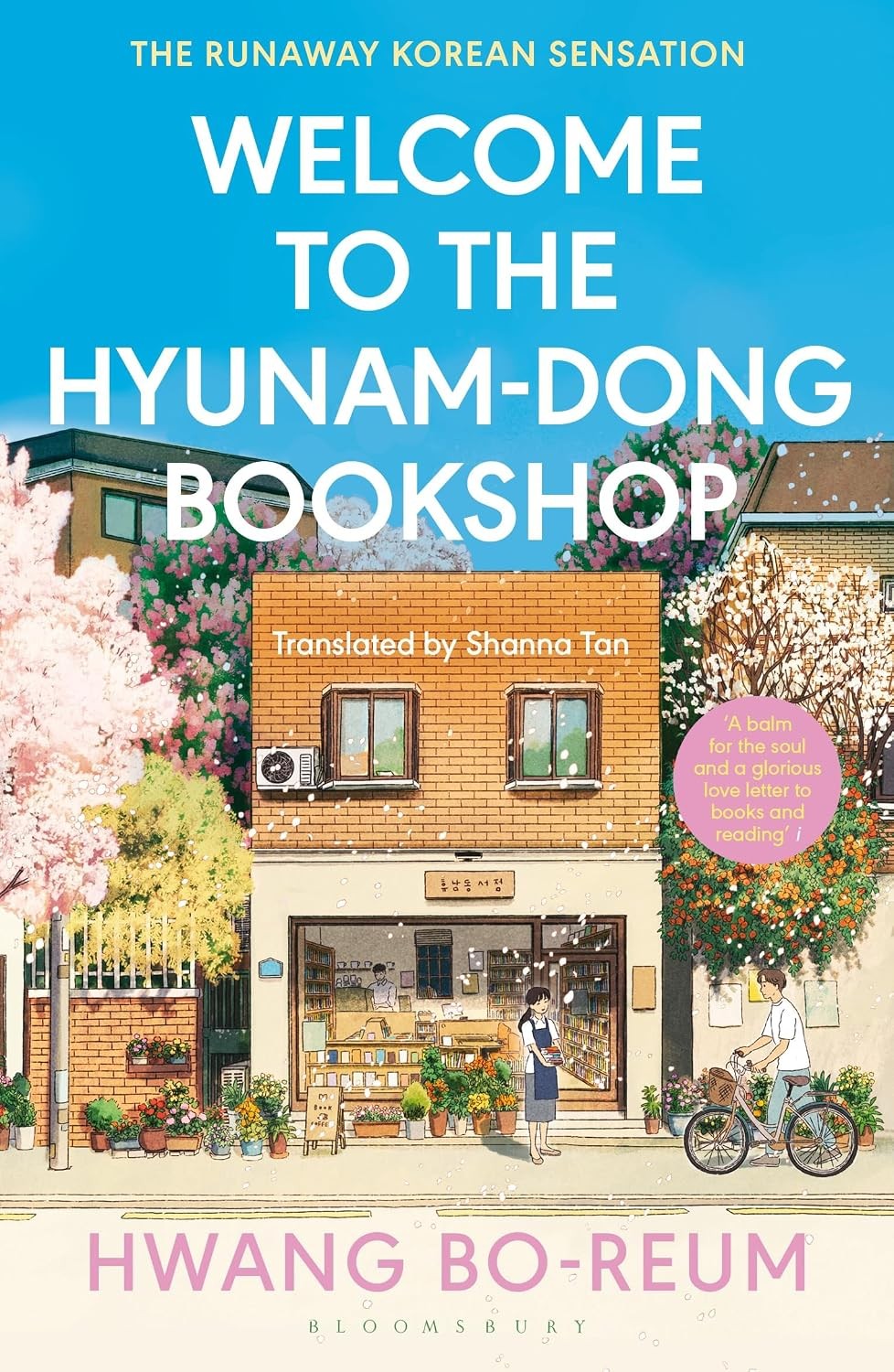 Buku novel Welcome to Hyunam-Dong Bookshop terbuka di meja kayu di samping cangkir kopi pour-over.