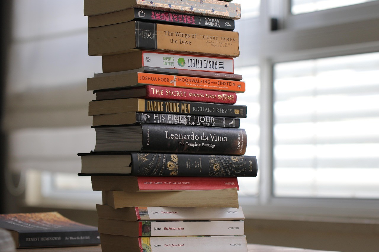 Karakter kaligrafi kanji Jepang '積ん読' (tsundoku) bersanding dengan buku-buku bersampul indah.